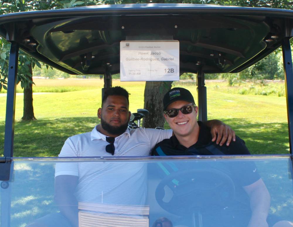 2 men in golf cart in the shade